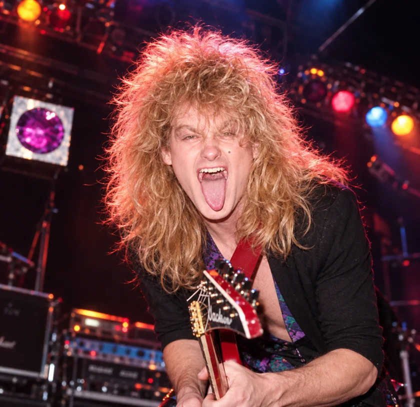 Larry on stage in 1986, big hair, tongue out, playing a red Jackson guitar
